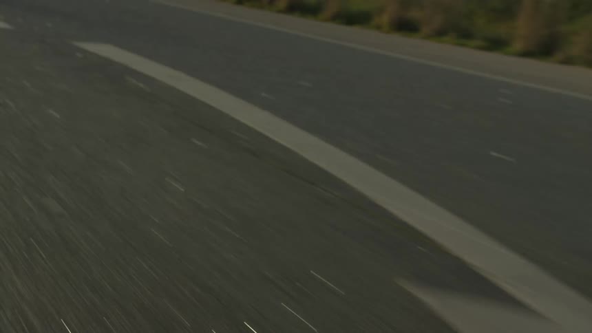 A fast-paced, point-of-view shot looking down at an asphalt road as the white lines and directional arrows blur past