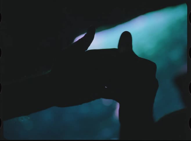 A tender moment captured on vintage film shows the silhouette of two hands gently caressing each other in a dark, moody setting