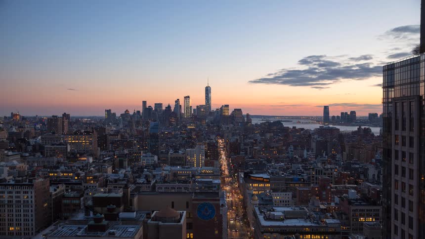 A stunning time-lapse of the downtown Manhattan skyline transitioning from a golden hour sunset to a vibrant night full of city lights