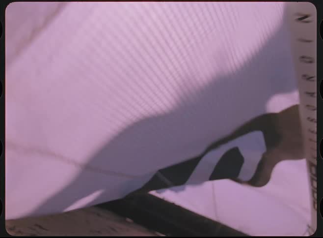 Vintage Super 8 film captures a close-up of a kitesurfing kite billowing in the wind on a sandy beach