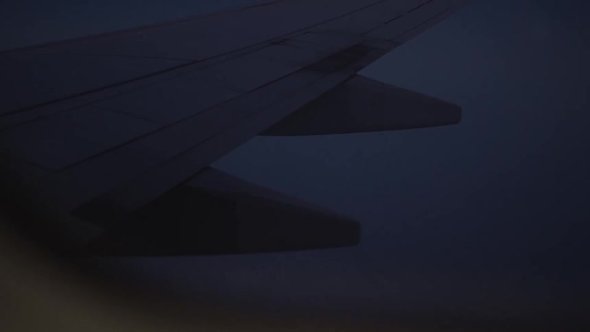 A static shot looking out an airplane window at the wing during a dark night flight