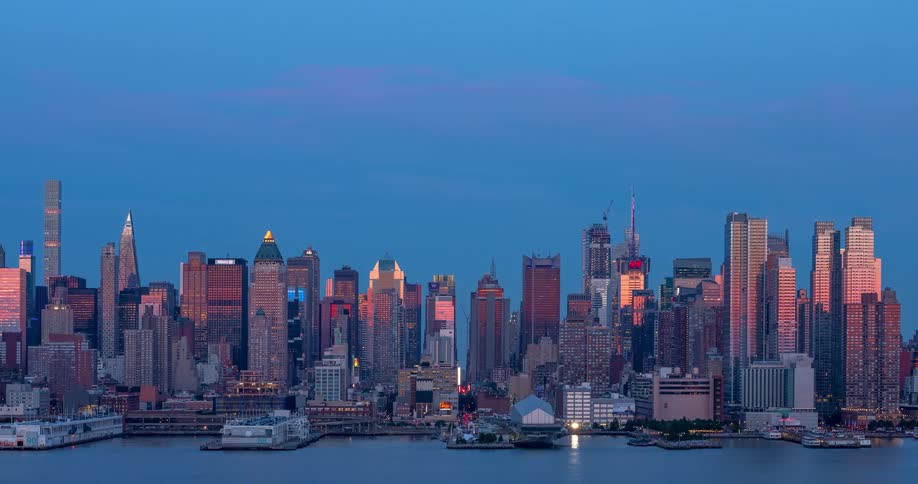 A timelapse of the Midtown Manhattan skyline as the sun sets, casting a warm glow on the buildings before the city lights illuminate the night sky