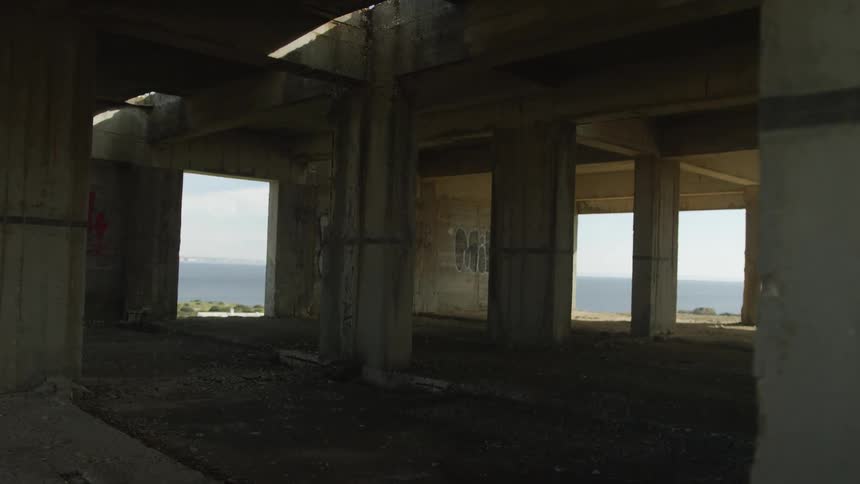 Tracking shot through the concrete pillars of an abandoned, graffiti-covered building with an ocean view