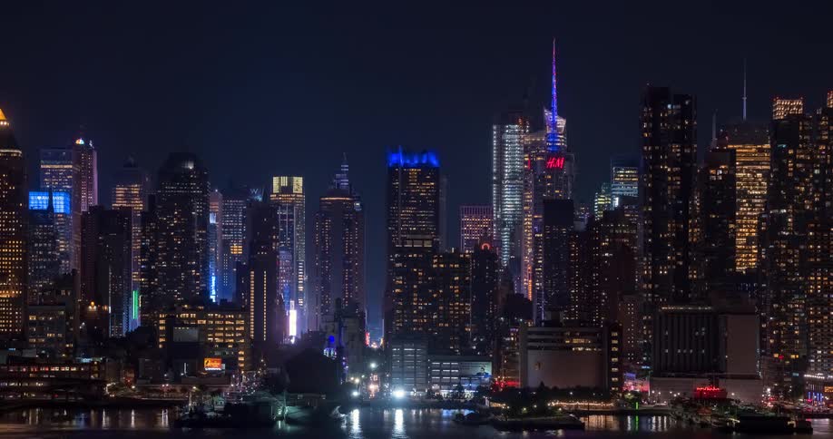A vibrant time-lapse of the New York City skyline at night, with skyscrapers and advertisements glowing brightly over the busy streets