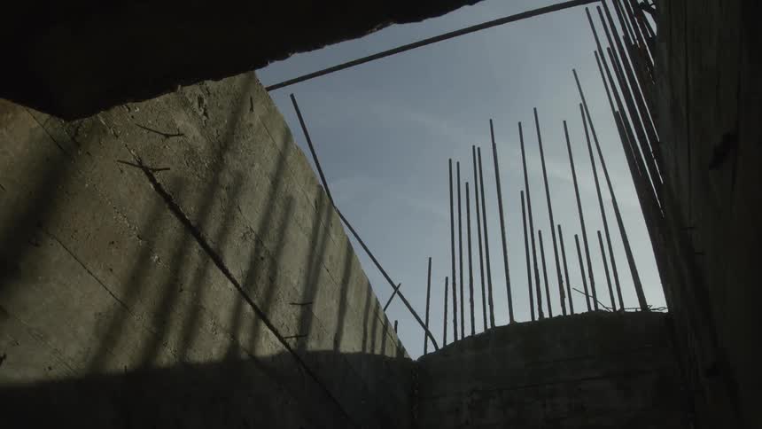 Low angle view from inside a dark, unfinished concrete structure with rebar silhouetted against the bright sky