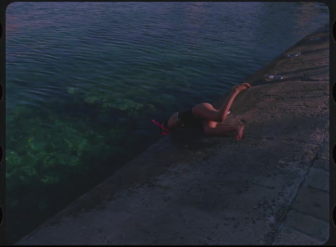 Vintage-style footage of a woman in a swimsuit and snorkel mask looking into the clear sea from a stone pier
