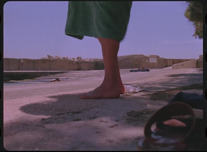A person changes into their swimsuit under a towel on a concrete pier in this vintage-style footage
