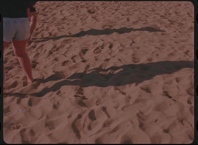 Vintage-style footage shows the moving shadows of people on a sandy beach during a sunny day