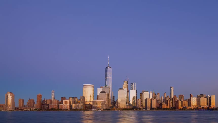 A breathtaking time-lapse captures the transition from a golden hour sunset to a sparkling night over the Lower Manhattan skyline and Hudson River