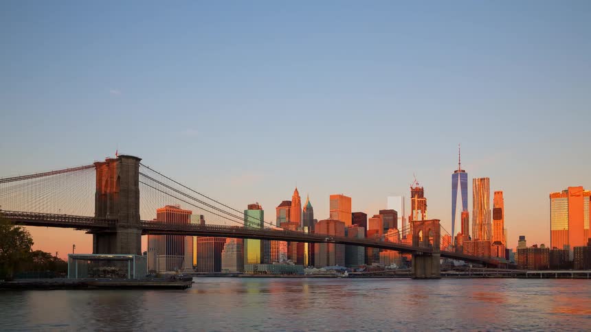 A stunning night-to-day timelapse captures the iconic Brooklyn Bridge and Manhattan skyline as the city awakens with a golden sunrise