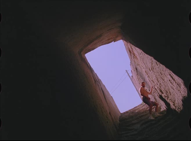 Low-angle vintage film shot of a man descending the rough steps into a deep, shadowy well