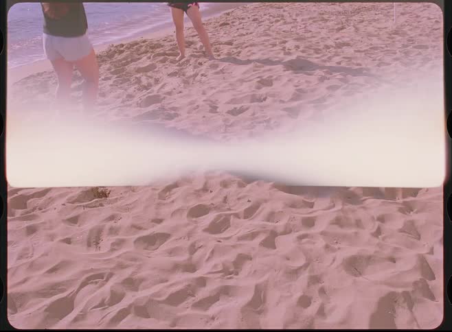 Retro home movie captures two friends playing with a ball on the sand by the ocean's edge