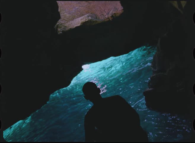A silhouetted person jumps into the glowing turquoise water of a secret grotto and floats on their back in slow motion