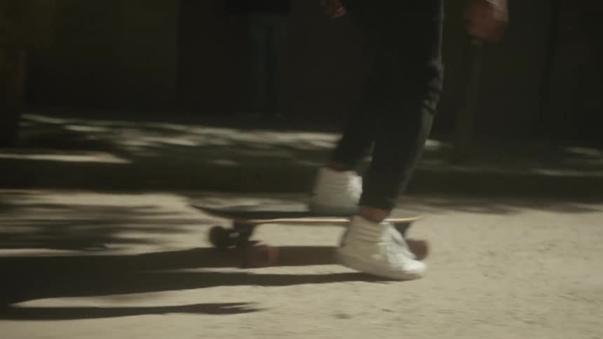 A close-up slow-motion shot of a person in white high-tops skateboarding on a longboard down a city street at night