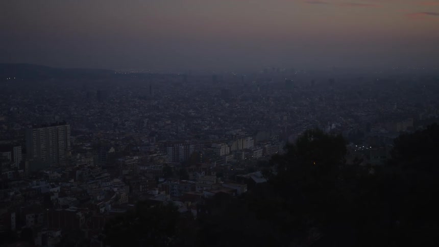 A vast and hazy city skyline at twilight, with the faint glow of city lights scattered across the urban landscape