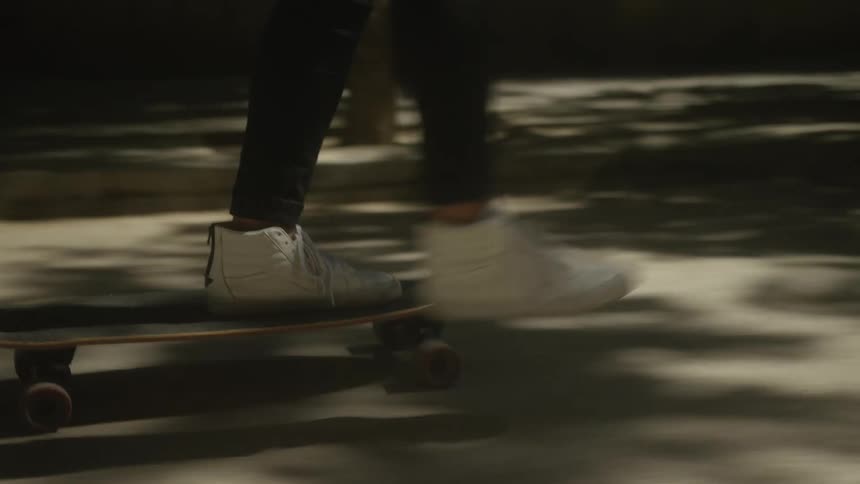 Close-up slow-motion shot of a person's feet in white sneakers pushing a longboard on a city sidewalk at night