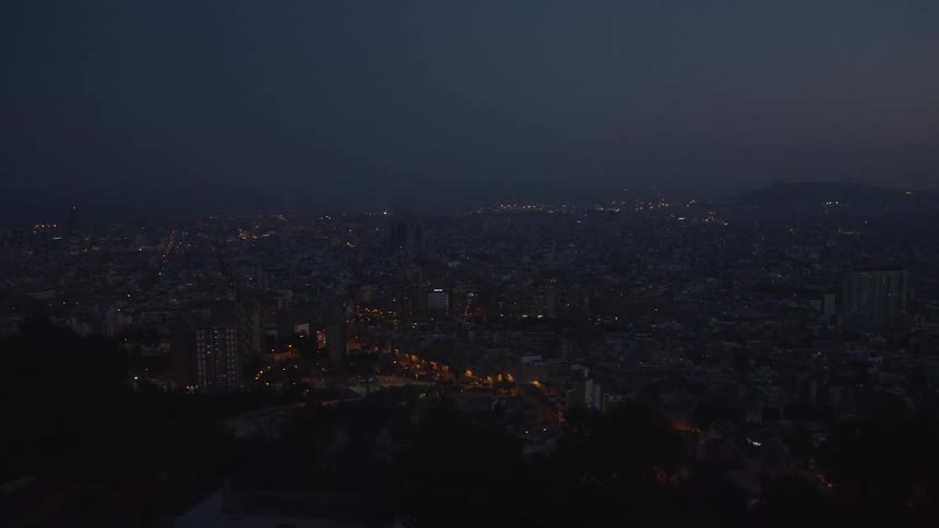 A wide, elevated view of a sprawling city at night with streets and buildings illuminated under a dark twilight sky