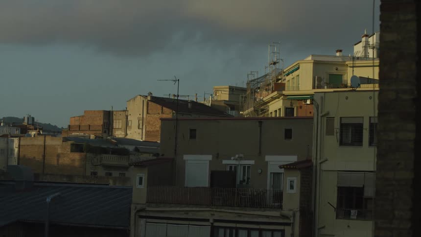 A static shot of European city rooftops bathed in golden hour light as clouds pass overhead