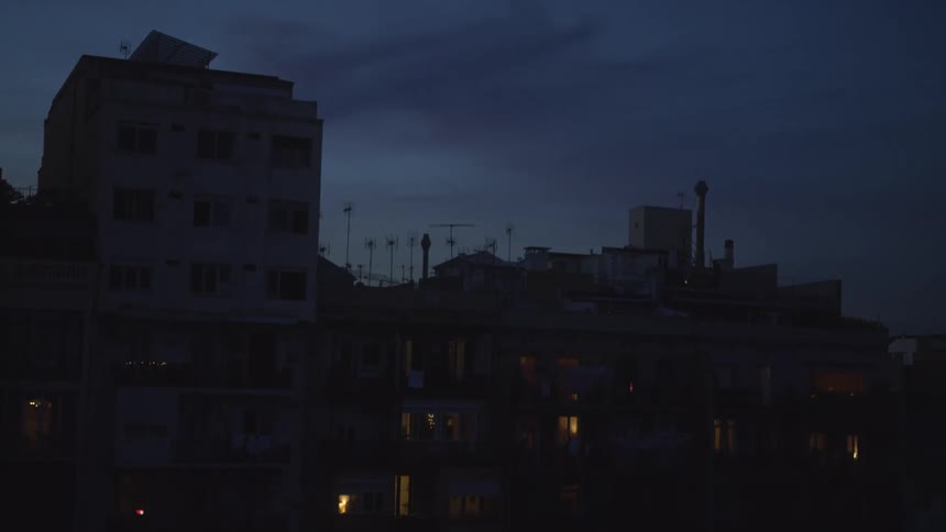 A quiet urban scene shows apartment buildings with lit windows against the pre-dawn sky