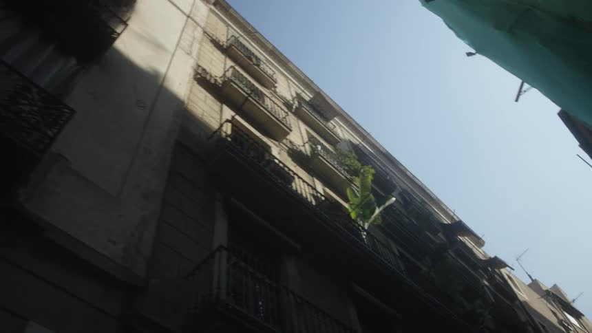 A low-angle view pans across a classic European apartment building as a white curtain billows in the wind on a shaded balcony