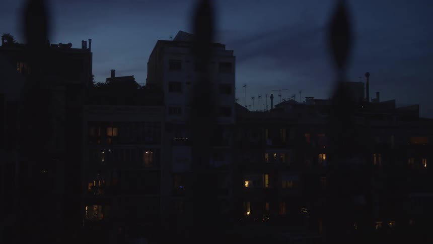 A slow pan reveals a dark city skyline at twilight, with the warm glow of lights from apartment windows