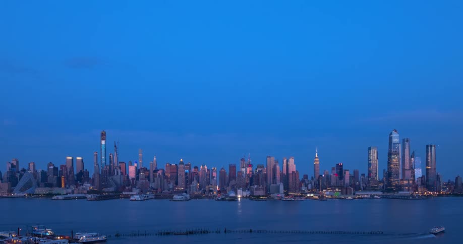 A stunning day-to-night timelapse of the Midtown Manhattan skyline with boats cruising on the Hudson River as the city lights up after sunset