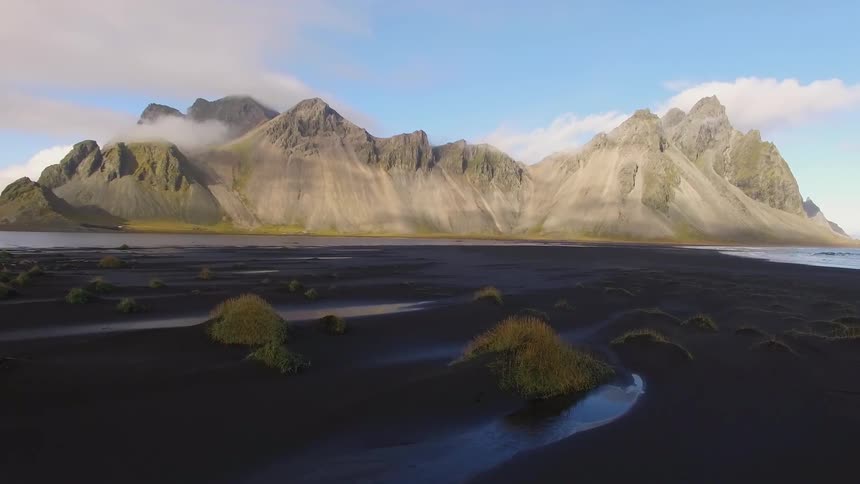 Floating over black sand beach dunes and grasses towards majestic mountains