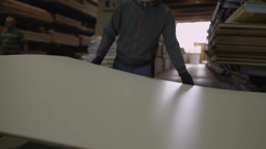 Slow motion shot of a worker in a warehouse carefully placing a large white building panel