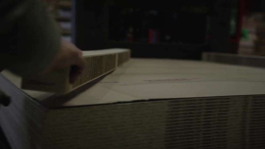 A factory worker carefully handles a large stack of particle boards in a dimly lit warehouse