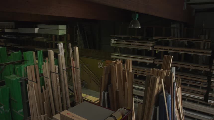 Panning shot reveals a large, dimly lit warehouse with neatly stacked lumber and various building materials on shelves