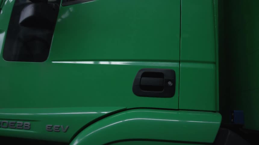 A close-up of a green commercial truck door closing automatically while parked inside a warehouse