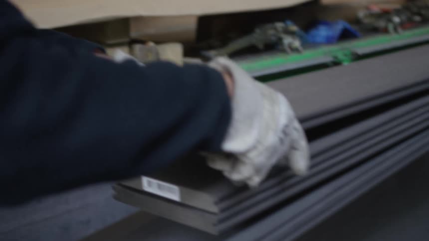 A factory worker wearing gloves carefully stacks newly manufactured composite planks on a production line