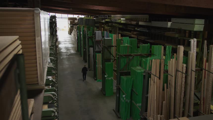 High angle view of a man walking through a large lumber warehouse filled with various types of wood