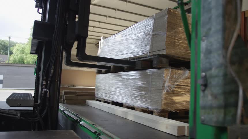 A forklift carefully loads wrapped pallets of construction materials into the back of a large transport truck