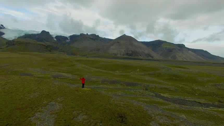 A person stands with their arms outstretched in a mountain valley