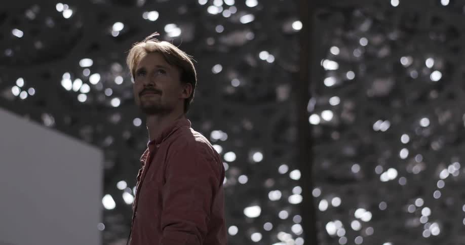 A man turns around under a dappled light roof
