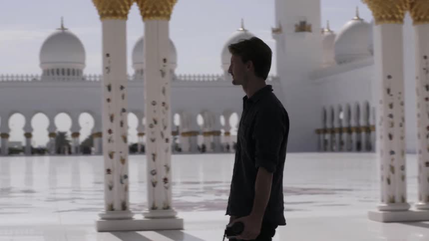 A man walks with his camera by a building