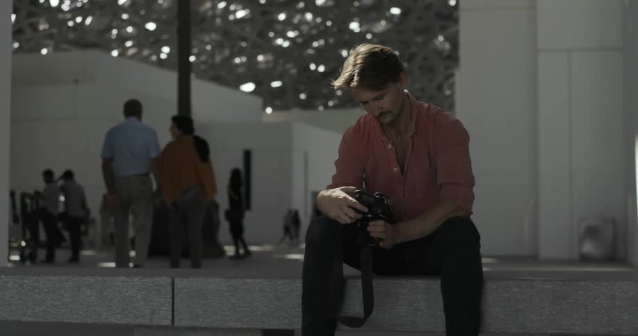 Man sits on a concrete ledge looking at his camera