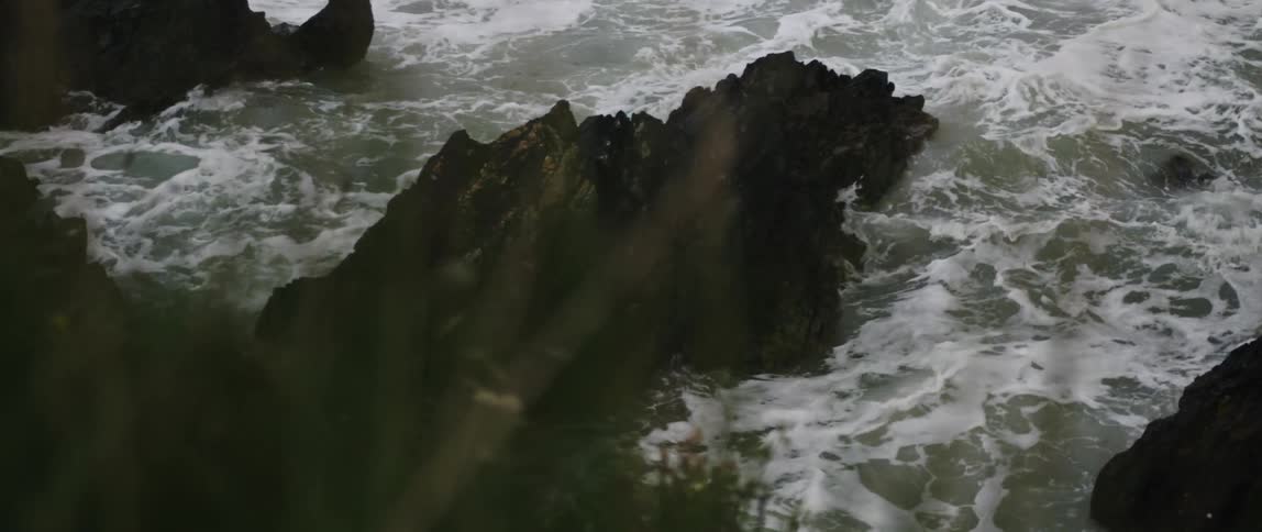 Ethereal light rays illuminate powerful ocean waves crashing against dark rocks on a stormy coast