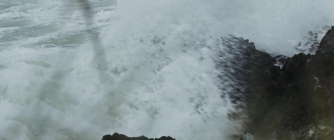 A powerful ocean wave crashes against a rugged coastal rock formation in dramatic slow motion