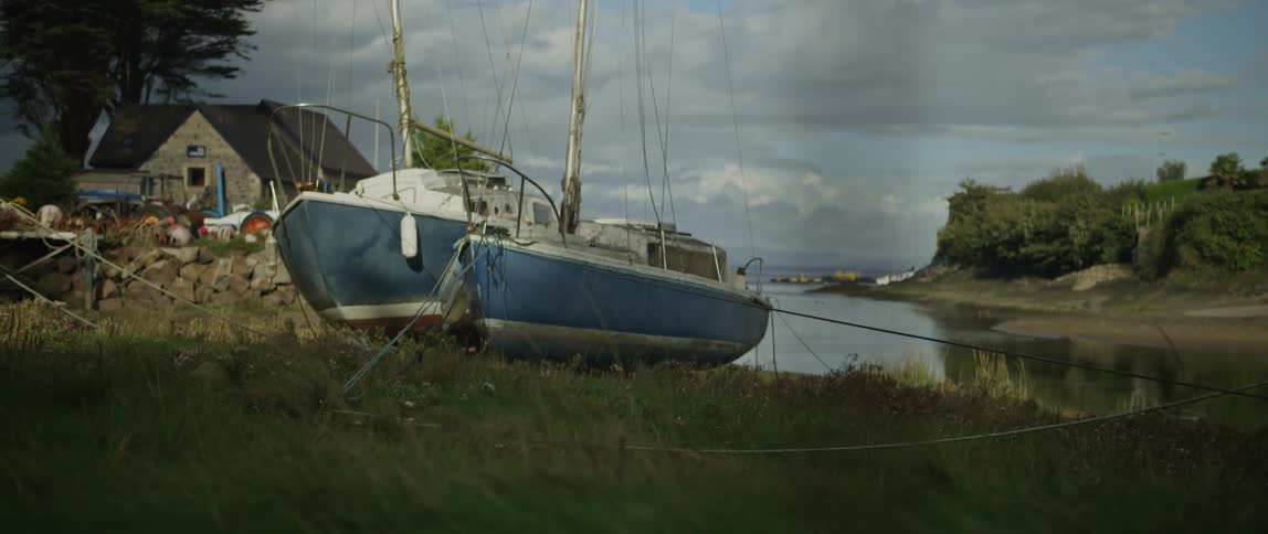 A serene shot of two sailboats moored on a grassy riverbank on a cloudy day