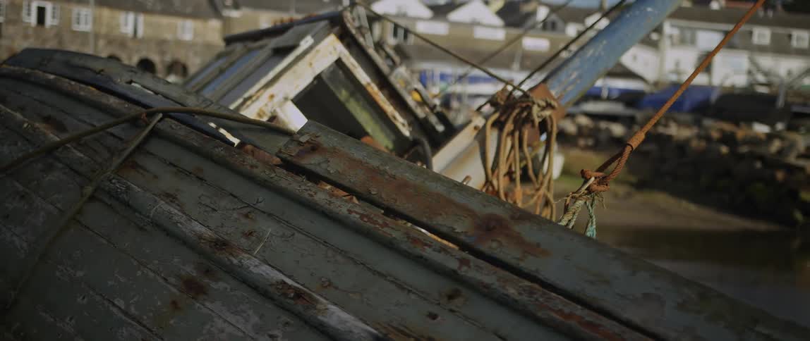Close up shot of a weathered and rusty old boat decaying in a harbor as the sun flares through a crack