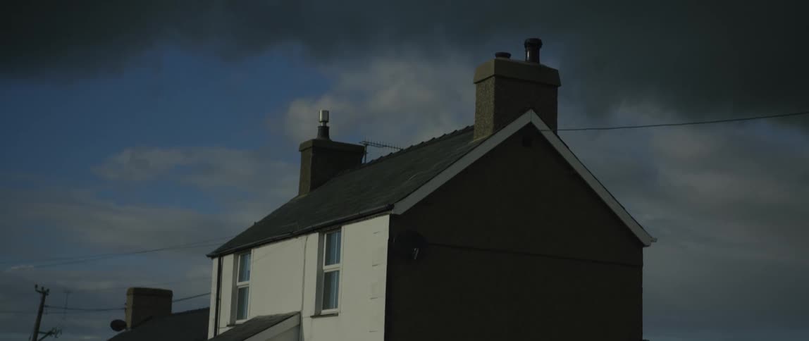A moody static shot of a house roofline under a dramatic, cloudy sky