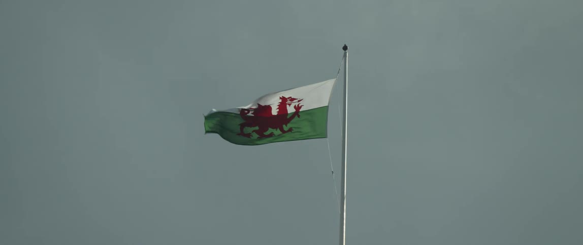 The Welsh national flag with the red dragon waves proudly in the wind against a cloudy sky