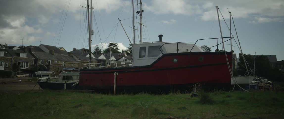 A weathered red and white boat sits on a grassy bank in a quiet coastal village