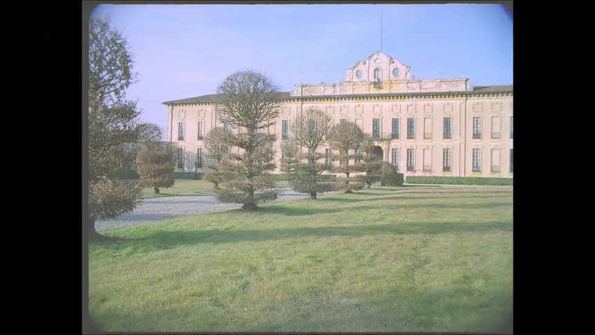 A nostalgic view of a grand Italian villa with manicured gardens and a wide lawn, captured on vintage Super 8 film