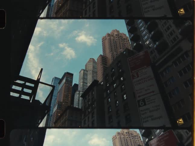 A vintage, low-angle shot of New York City skyscrapers against a blue sky, framed by the film strip itself as a bird flies by