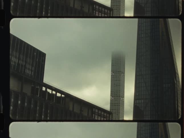 A moody 16mm film shot captures the top of a modern skyscraper vanishing into a thick blanket of fog on a gloomy day in the city