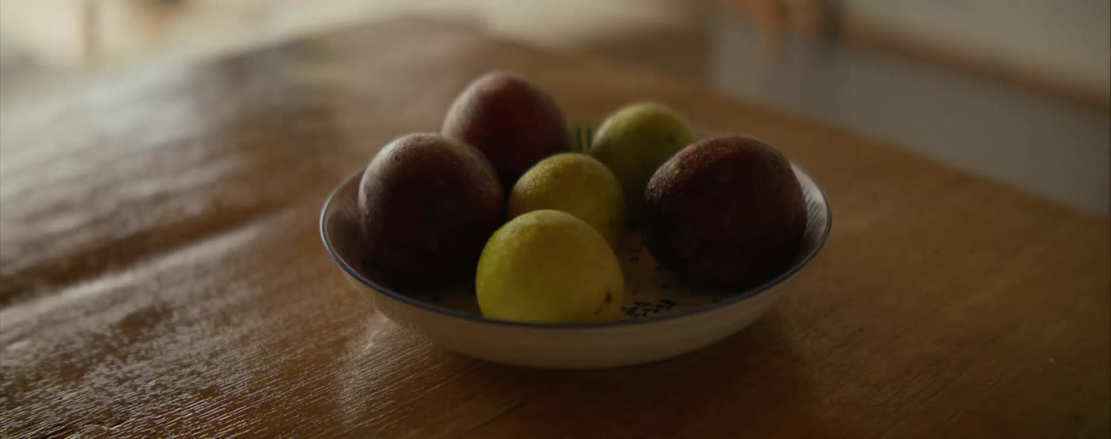 A close-up still life shot of a bowl of fresh passion fruit sitting on a wooden table in natural light