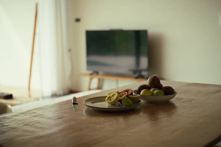 Freshly sliced passion fruit sits on a plate next to a bowl of whole fruits on a wooden dining table